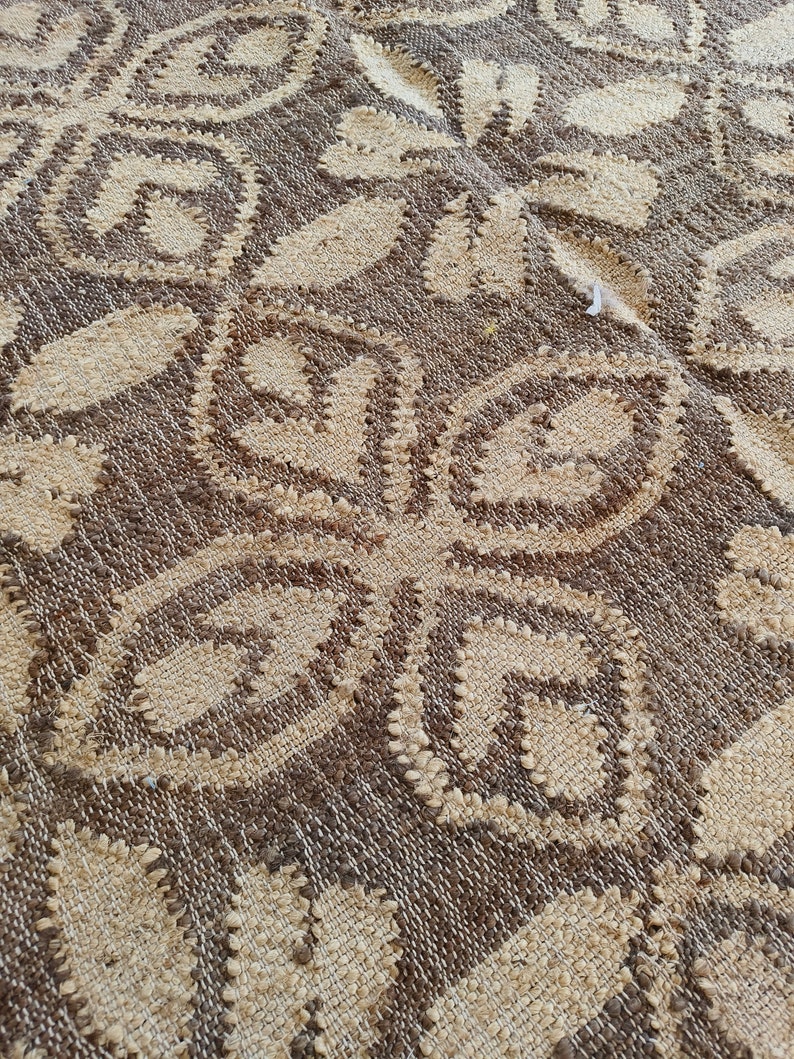 May include: Close-up of a woven rug with a brown and beige pattern. The rug has a textured surface and a repeating design of interlocking circles.