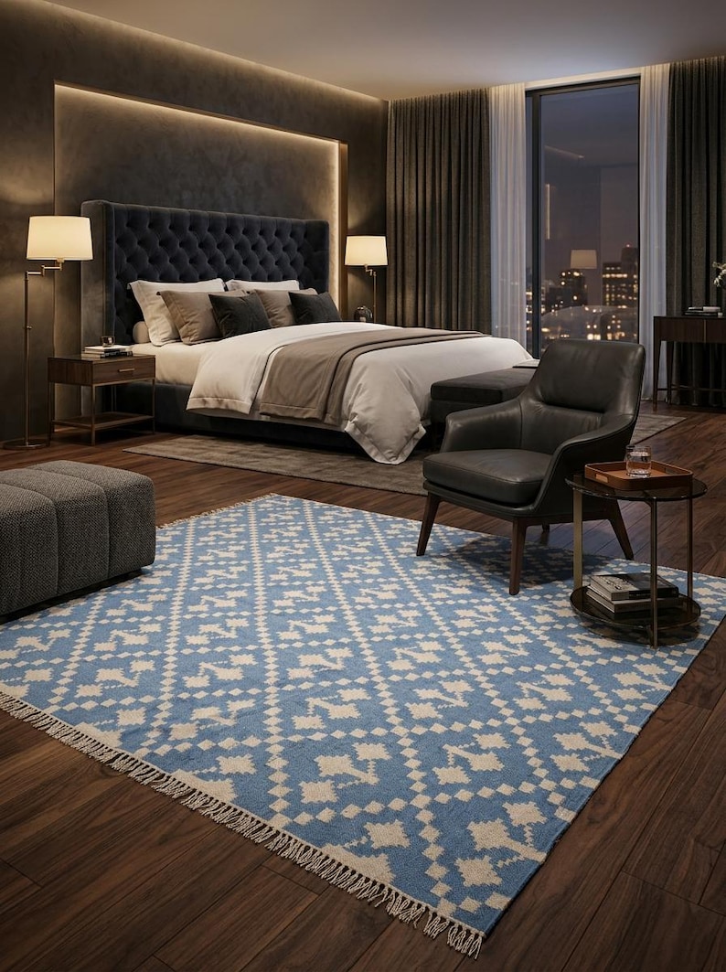 Puede incluir: Dormitorio con una cama grande, una alfombra estampada azul y blanca y un sill&oacute;n de cuero. La habitaci&oacute;n tiene suelo de madera oscura, una ventana grande y una iluminaci&oacute;n suave. La alfombra tiene un dise&ntilde;o geom&eacute;trico.