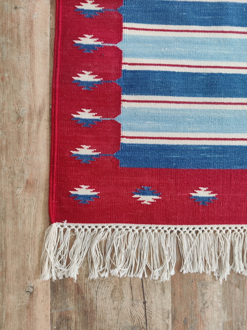 May include: A red, blue, and white striped rug with a fringe border. The rug has a geometric pattern in the border.