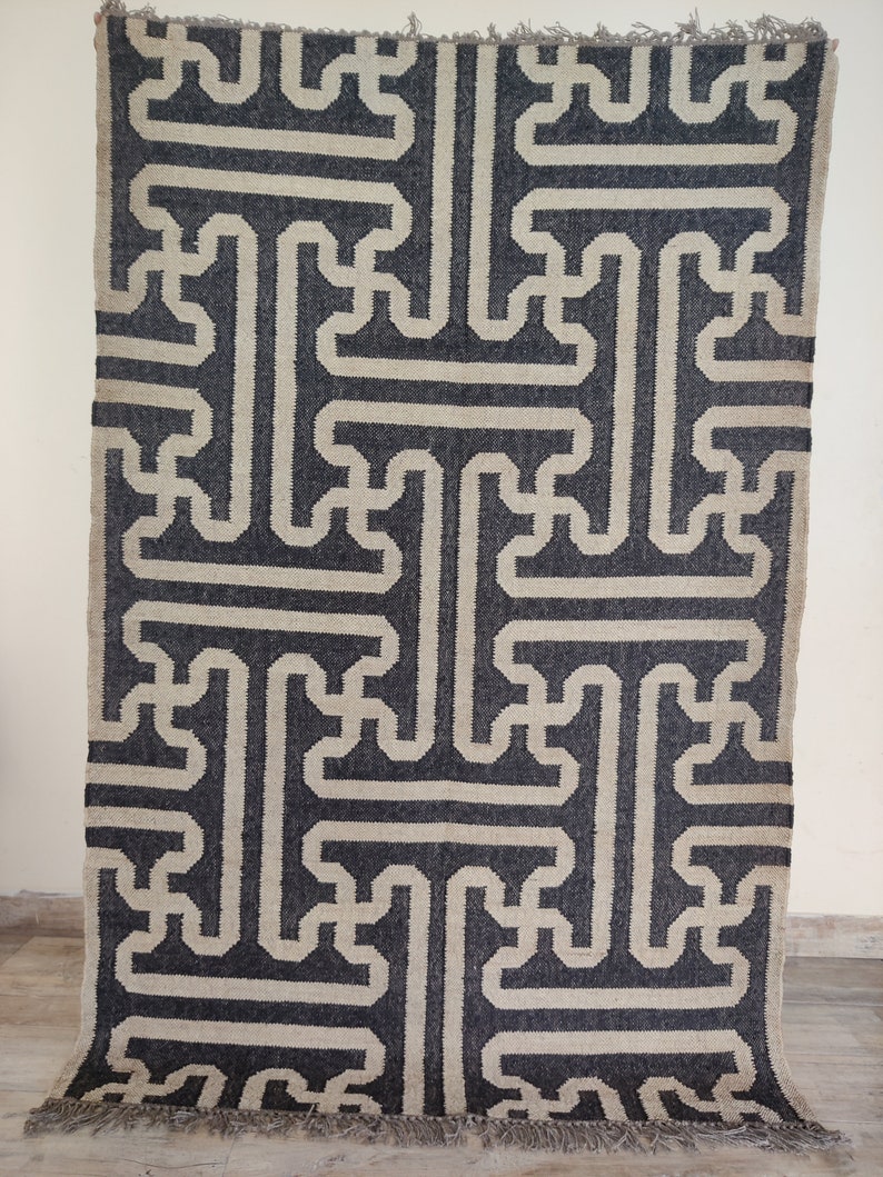 Może przedstawiać: Geometriczny dywan w czarno-białe wzory z frędzlami. Dywan ma prosty, nowoczesny design.