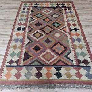 May include: A colorful rug with a geometric pattern in shades of red, orange, green, brown, and black. The rug has a fringe border.