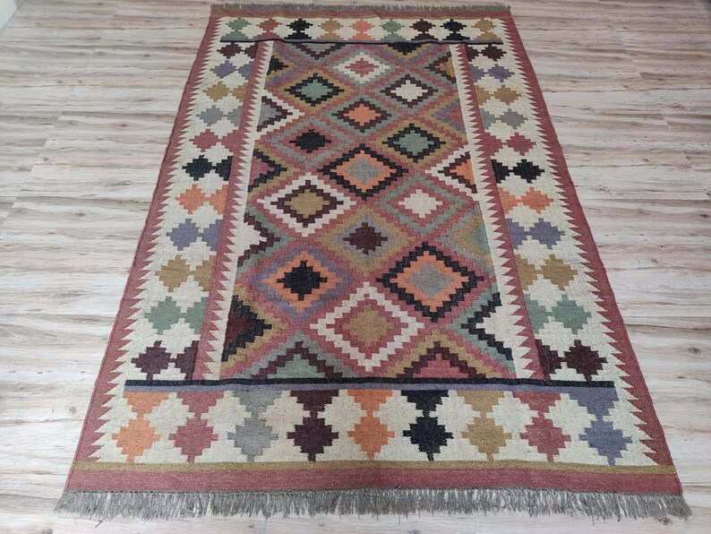 May include: A colorful rug with a geometric pattern in shades of red, orange, green, brown, and black. The rug has a fringe border.