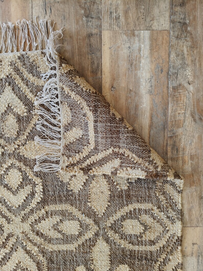 May include: A brown and beige patterned rug with fringe on the edges. The rug is folded over on a wooden floor.