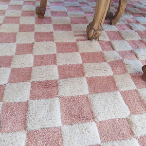 Puede incluir: Una alfombra de cuadros rosa y blanco con una textura esponjosa. La alfombra está hecha de un material suave y mullido y tiene un patrón de tablero de ajedrez.