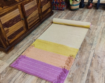 May include: A multi-colored yoga mat with fringe detailing. The mat is rolled up and has a light beige, yellow, peach, and purple color scheme.