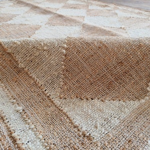 Pu&ograve; includere: Un tappeto tessuto con un motivo a scacchi beige e bianco. Il tappeto &egrave; realizzato in fibre naturali e ha una superficie testurizzata.