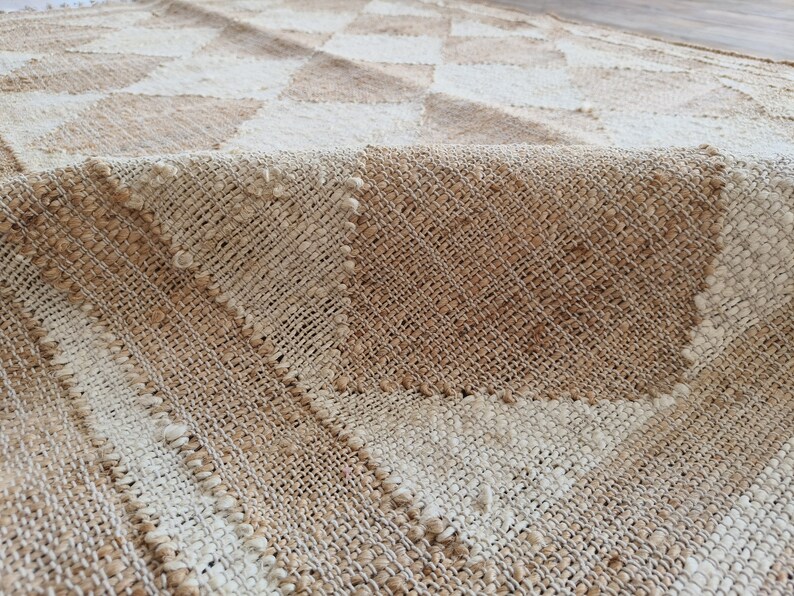 Pu&ograve; includere: Un tappeto tessuto con un motivo a scacchi beige e bianco. Il tappeto &egrave; realizzato in fibre naturali e ha una superficie testurizzata.