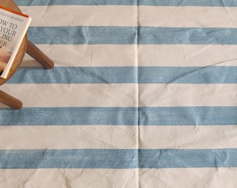 Peut inclure: Un tapis rayé blanc et bleu avec un livre intitulé "How to Sell Your Writing" sur un tabouret en bois.