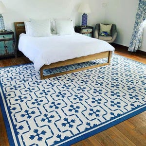 May include: A white bed with a blue and white patterned rug. The bed has a white duvet and two white pillows. The rug has a geometric pattern with blue and white squares.