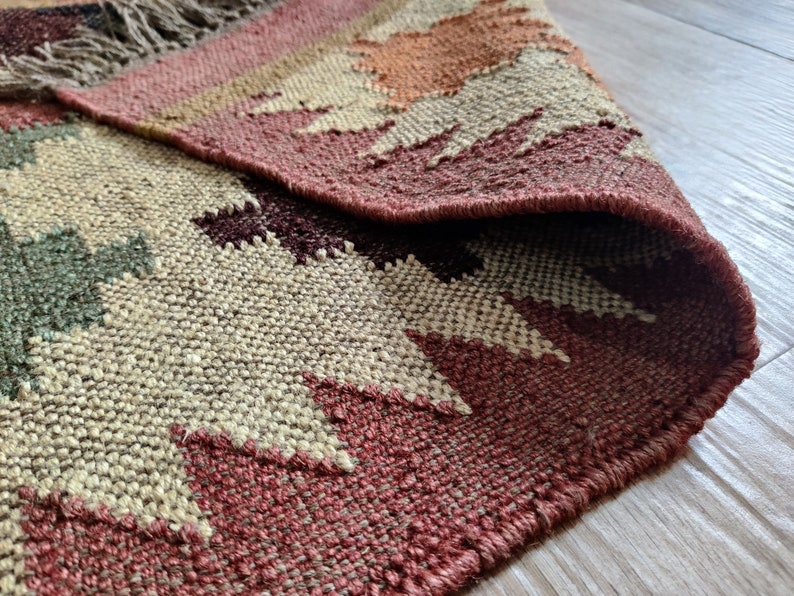 May include: A woven rug with a geometric pattern in shades of brown, beige, and red. The rug has a fringed edge and is made of natural fibers.