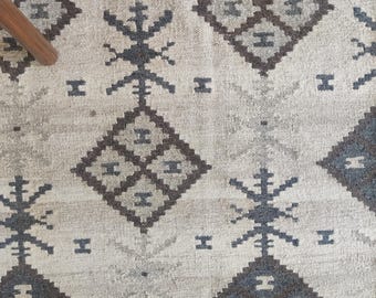 May include: A beige rug with a geometric pattern in shades of brown and blue. The pattern features repeating diamond shapes and stylized snowflakes.