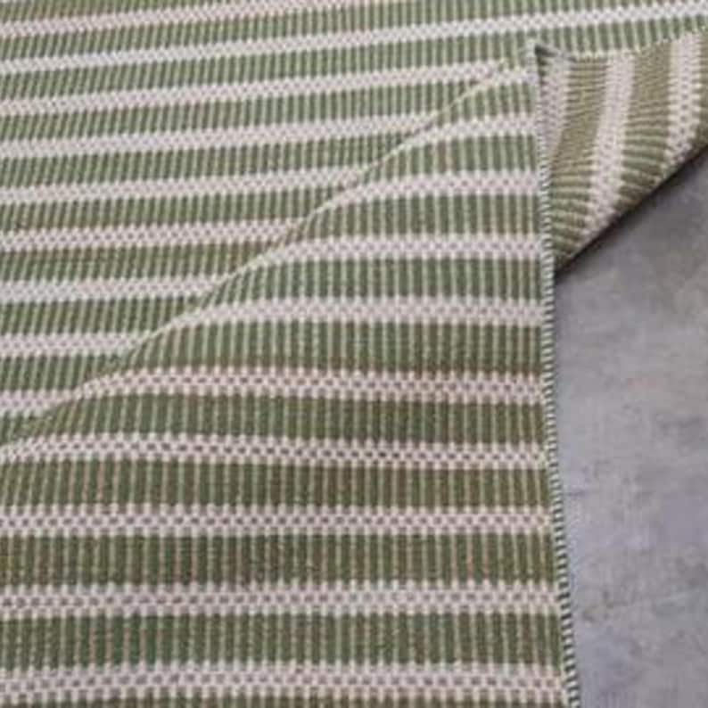 May include: Close-up of a green and white striped rug with a woven texture. The rug is folded over, showing the underside.
