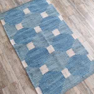Könnte beinhalten: Ein blauer und weißer gewebter Teppich mit geometrischem Muster. Der Teppich hat ein kariertes Design mit weißen Quadraten und blauen Kreisen.