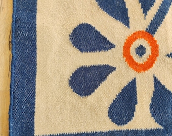 Könnte beinhalten: Nahaufnahme eines cremefarbenen Teppichs mit blauem Rand und einem großen blauen und orangefarbenen Blumendesign.