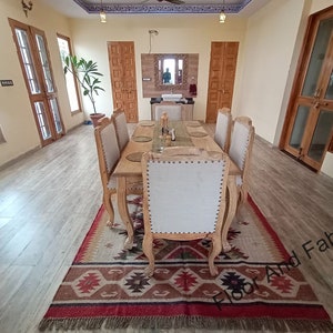 May include: A wooden dining table set with six chairs, a rug with a geometric pattern, and a mirror on the wall. The table is set with placemats and silverware.