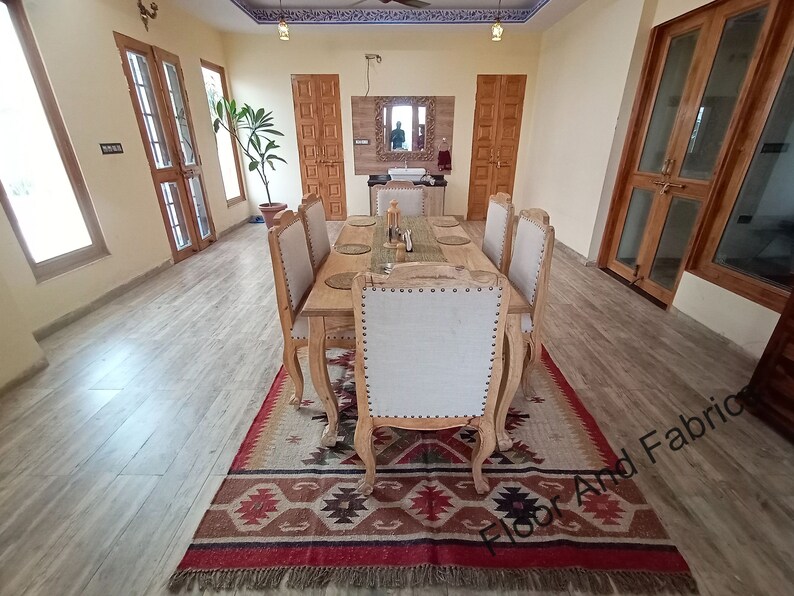 May include: A wooden dining table set with six chairs, a rug with a geometric pattern, and a mirror on the wall. The table is set with placemats and silverware.