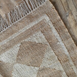 Pu&ograve; includere: Un tappeto in fibra naturale con un motivo geometrico in tonalit&agrave; beige e bianco. Il tappeto ha un bordo a frangia.
