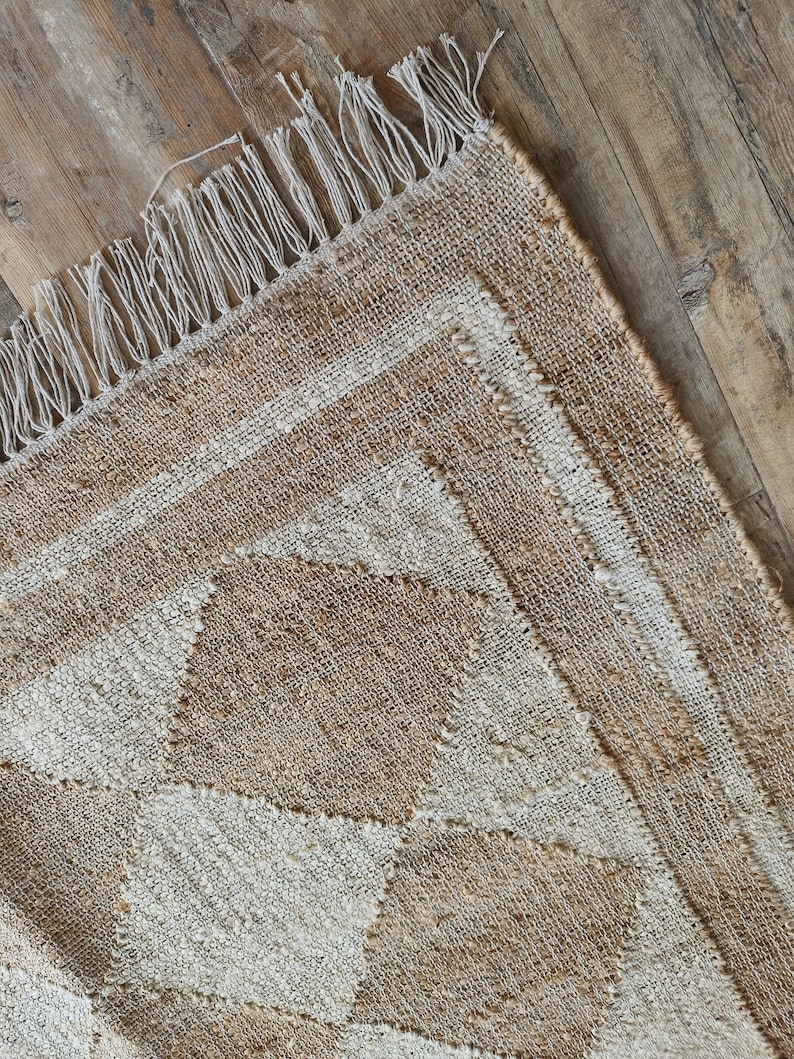 Pu&ograve; includere: Un tappeto in fibra naturale con un motivo geometrico in tonalit&agrave; beige e bianco. Il tappeto ha un bordo a frangia.