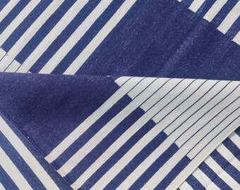 Puede incluir: Un textil doblado con un patrón geométrico de rayas diagonales blancas y azul marino alternas. La tela está doblada, revelando el reverso con una sección azul marino sólida y una continuación del diseño a rayas.