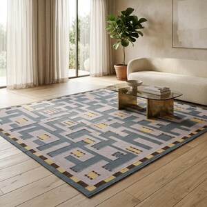 May include: A large rectangular area rug featuring a geometric pattern in shades of slate blue, light gray, and mustard yellow. The design consists of interlocking blocks and lines, with a dark brown border accenting the edges of the rug.