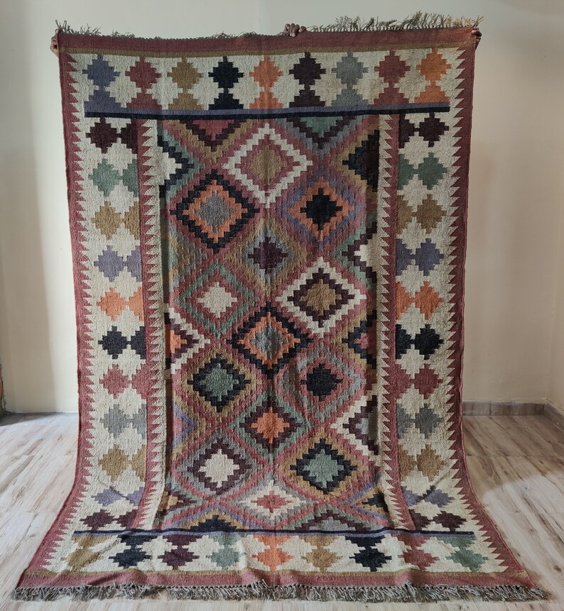 May include: A colorful handwoven rug with a geometric pattern in shades of brown, red, orange, green, and black. The rug has a fringe border.