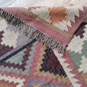 May include: A colorful, geometric patterned rug with a fringe border. The rug is made of natural fibers and has a rustic, hand-woven look.