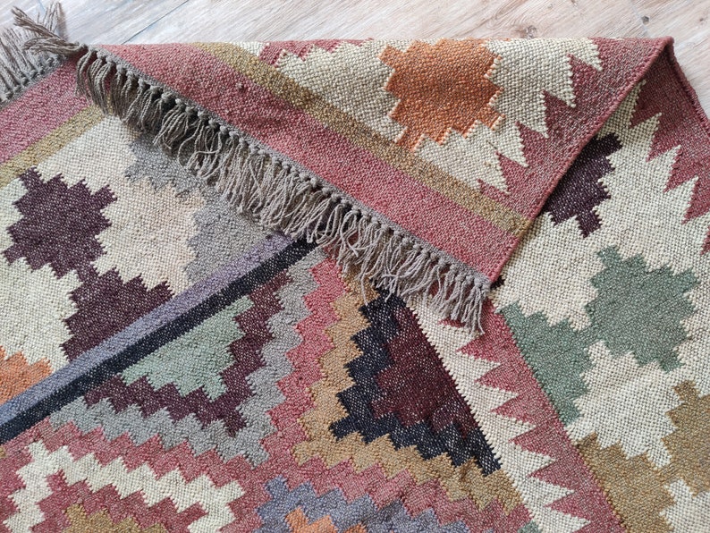 May include: A colorful, geometric patterned rug with a fringe border. The rug is made of natural fibers and has a rustic, hand-woven look.