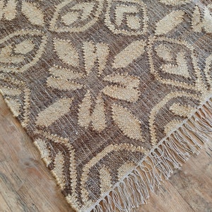 May include: A brown and cream woven rug with a geometric pattern and fringe on the edges.