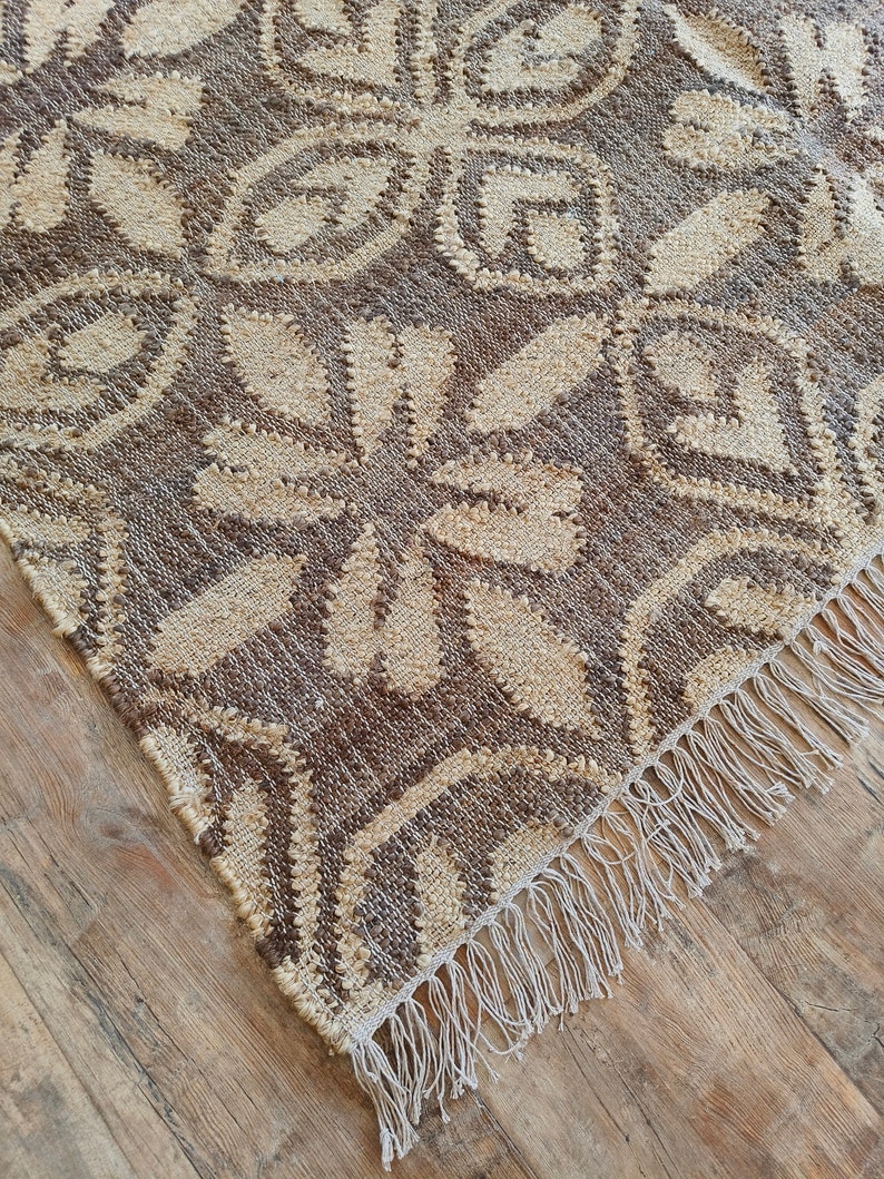 May include: A brown and cream woven rug with a geometric pattern and fringe on the edges.