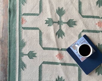 May include: A white and green patterned rug with a geometric design. The rug has a green border and a cream background. A blue notebook with the text "Creative Diary" is on top of the rug.