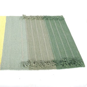 May include: A green and yellow striped rug with a fringe border. The rug is made of a woven material and has a subtle ombre effect.