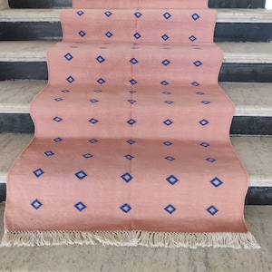 Puede incluir: Una alfombra de color rosa y azul con flecos en el borde inferior. La alfombra está colocada en una escalera.