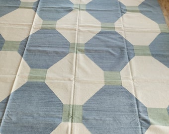 May include: A cream-colored rug with a geometric pattern of blue and green octagons. The rug has a fringe border.