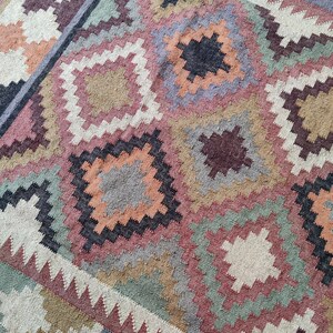 May include: A colorful rug with a geometric pattern in shades of brown, orange, pink, green, and gray. The rug is woven with a variety of textures and has a distressed look.
