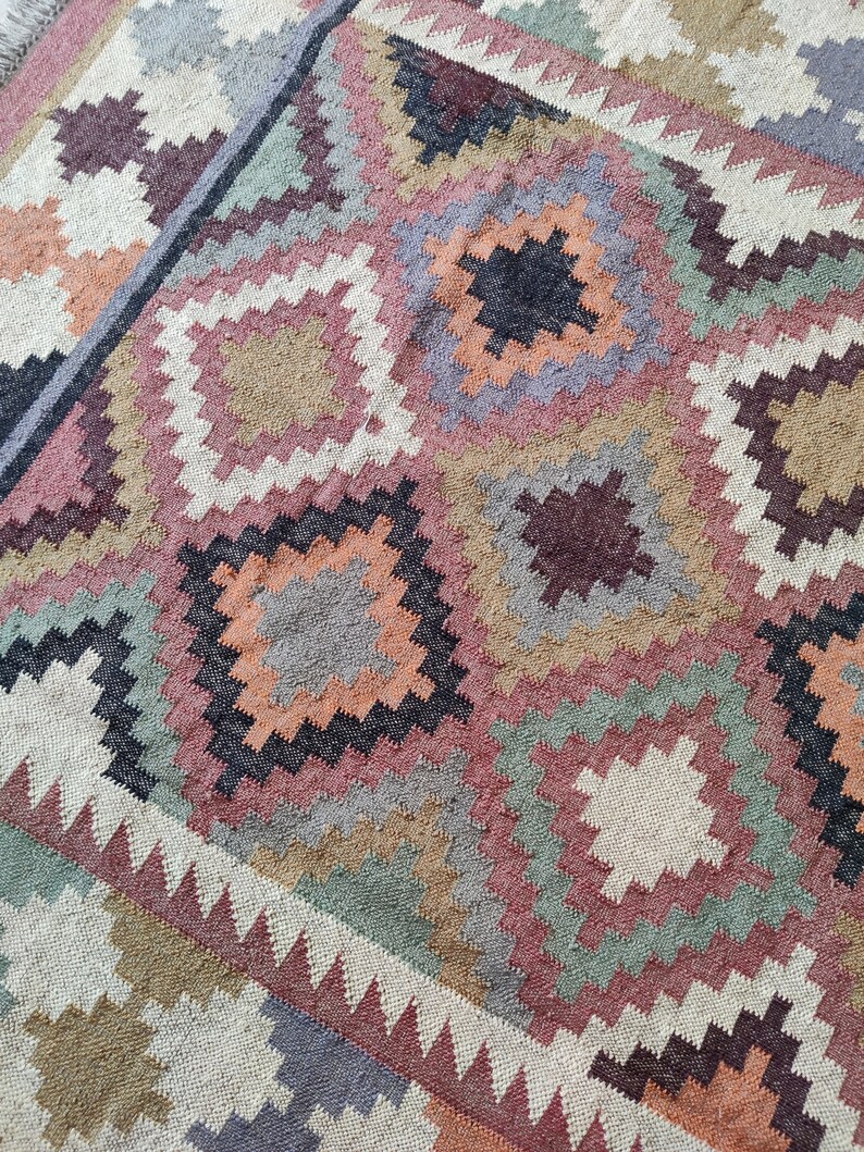 May include: A colorful rug with a geometric pattern in shades of brown, orange, pink, green, and gray. The rug is woven with a variety of textures and has a distressed look.