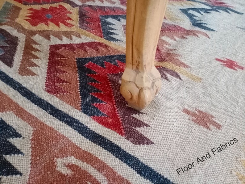 May include: A wooden table leg with a carved claw foot resting on a multi-colored patterned rug. The rug has a geometric design with shades of red, brown, black, and white. The text "Floor And Fabrics" is visible in the lower right corner of the image.