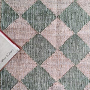 Pode incluir: Um close-up de um tapete tecido com um padrão xadrez em tons de bege e verde. O tapete tem um design em forma de diamante.