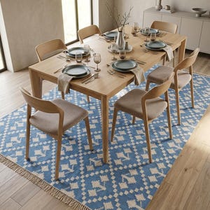 Puede incluir: Un juego de comedor con una mesa de madera clara y seis sillas a juego. La mesa est&aacute; puesta con platos, cubiertos y copas. Una alfombra azul y blanca estampada est&aacute; debajo de la mesa, y un jarr&oacute;n con ramas est&aacute; en el centro.