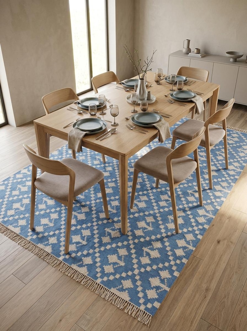 Puede incluir: Un juego de comedor con una mesa de madera clara y seis sillas a juego. La mesa est&aacute; puesta con platos, cubiertos y copas. Una alfombra azul y blanca estampada est&aacute; debajo de la mesa, y un jarr&oacute;n con ramas est&aacute; en el centro.