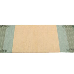 May include: A rectangular woven rug with a light beige center and green and blue stripes on the ends. The rug has a fringed edge.