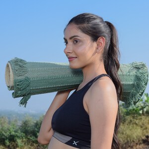 May include: A woman wearing a black sports bra with a white stripe and a green yoga mat slung over her shoulder.
