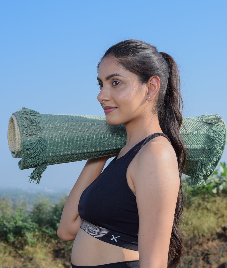 May include: A woman wearing a black sports bra with a white stripe and a green yoga mat slung over her shoulder.