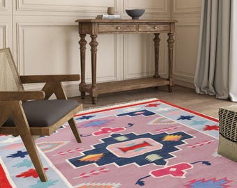 Puede incluir: Una alfombra de color rosa, azul y rojo con un diseño geométrico. La alfombra tiene un borde azul claro con detalles blancos y rojos.