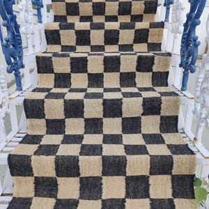 Puede incluir: Alfombra a cuadros negros y beige hecha de yute tejido. La alfombra está colocada en un conjunto de escaleras blancas con barandillas azules.