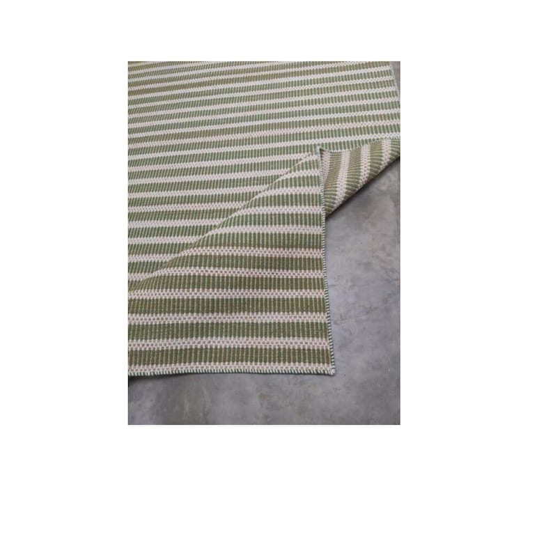 May include: A green and white striped rug with a woven texture. The rug is folded in half, showing the underside.
