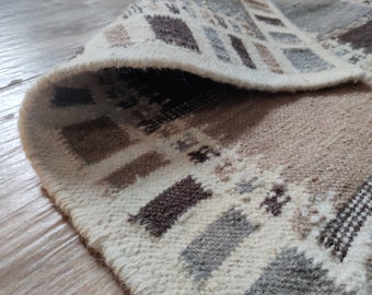 Könnte beinhalten: Nahaufnahme eines weißen, braunen und grauen gemusterten Teppichs mit geometrischem Design. Der Teppich ist umgeklappt und zeigt die Textur des Stoffes.