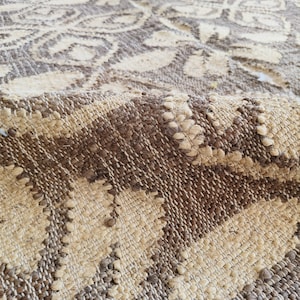 May include: Close-up of a woven rug with a brown and cream pattern. The rug has a textured surface and is made of natural fibers.