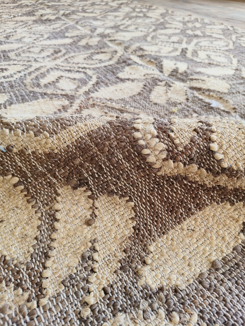 May include: Close-up of a woven rug with a brown and cream pattern. The rug has a textured surface and is made of natural fibers.
