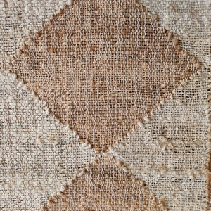Pu&ograve; includere: Primo piano di un tessuto tessuto con un motivo a rombi. Il tessuto &egrave; realizzato con fibre naturali e ha un colore marrone chiaro e beige.