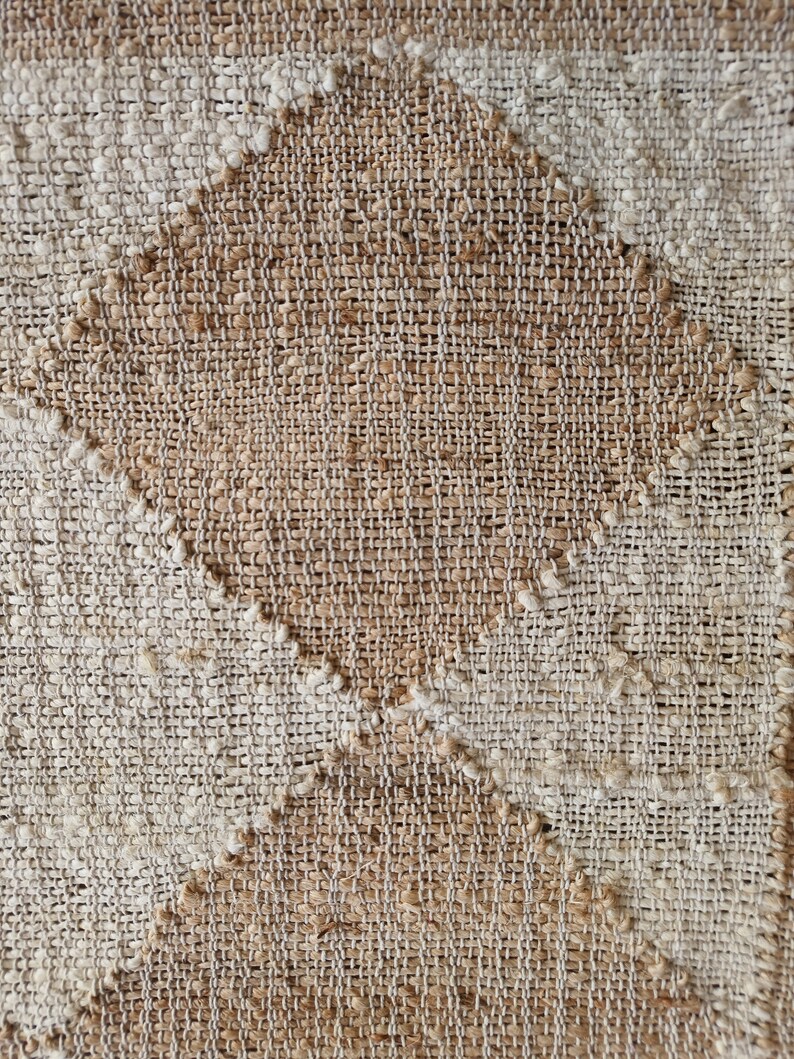 Pu&ograve; includere: Primo piano di un tessuto tessuto con un motivo a rombi. Il tessuto &egrave; realizzato con fibre naturali e ha un colore marrone chiaro e beige.